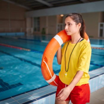 Close-up of female lifeguard walking with lifebuoy in indoor pool