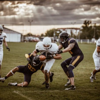 Determined American football player making a touchdown while passing through defensive players on playing field.
